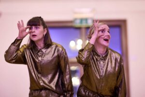 2 female performers dressed in shiny gold shirts.